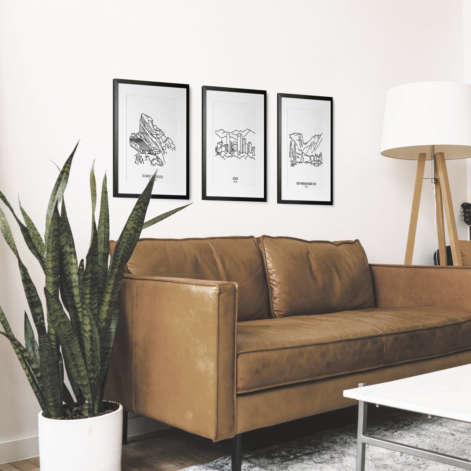 A group of three framed drawings on a wall above a couch with a potted plant