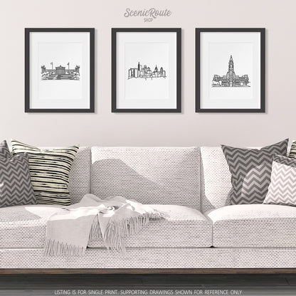 A group of three framed drawings on a wall hanging above a couch with pillows and a blanket. The line art drawings include the Philadelphia Art Museum, the Philadelphia Skyline, and Philadelphia City Hall