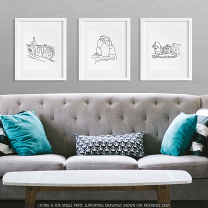 A group of three framed drawings on a wall above a couch. The line art drawings include Bryce Canyon National Park, Arches National Park, and Zion National Park