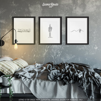A group of three framed drawings on a concrete wall above a messy bed. The line art drawings include the Phoenix Skyline, Saguaro Cactus, and Camelback Mountain