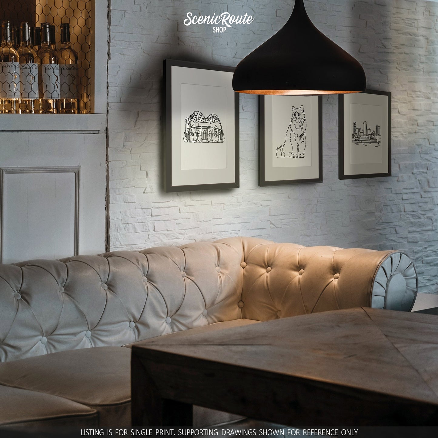 A group of three framed drawings on a white brick wall above a couch. The line art drawings include the Milwaukee Brewers Ballpark, a Birman cat, and the Milwaukee Skyline