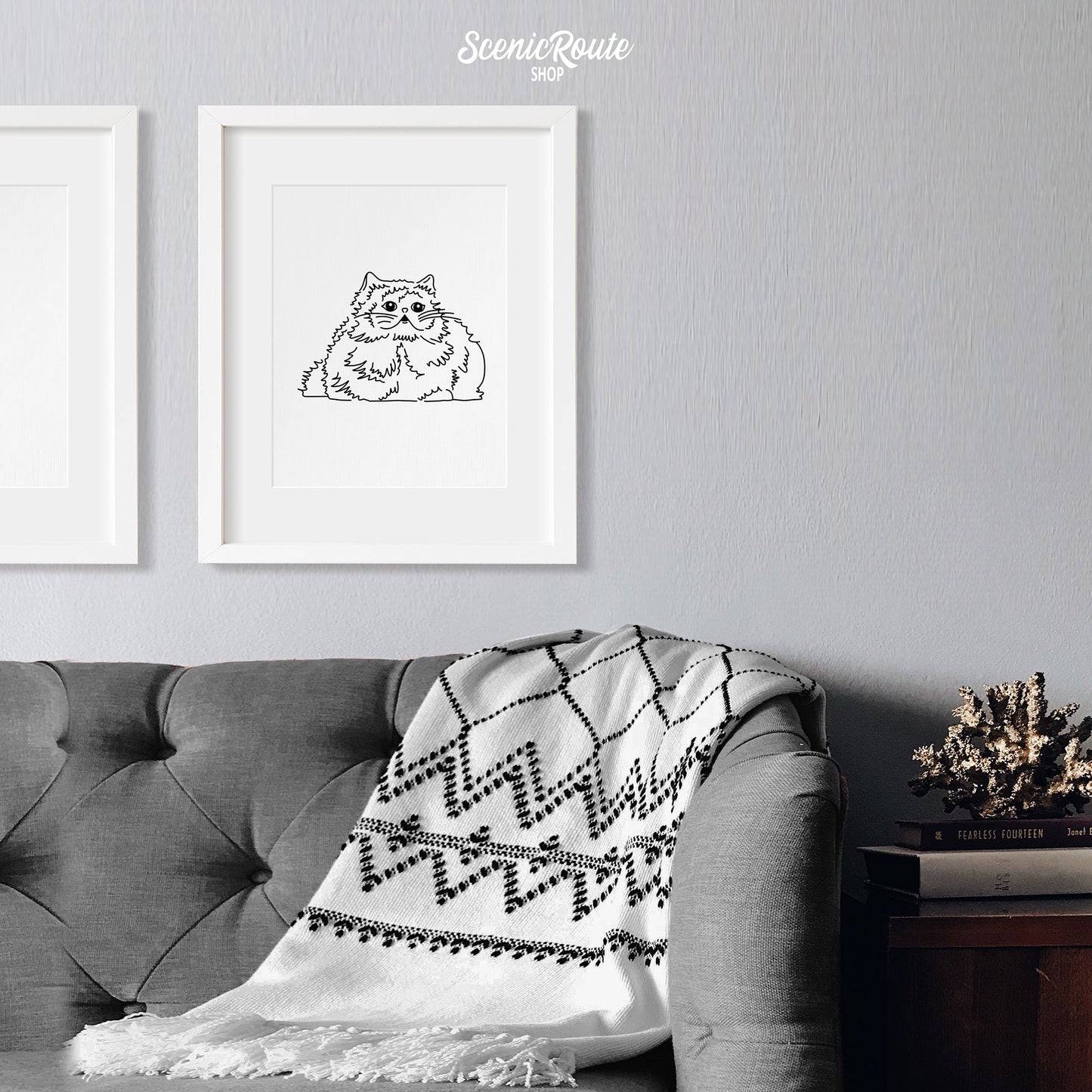 A framed line art drawing of a Himalayan cat above a couch with a blanket