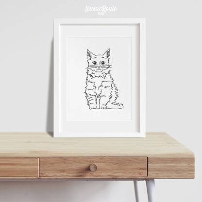 A framed line art drawing of a Maine Coon cat on a desk
