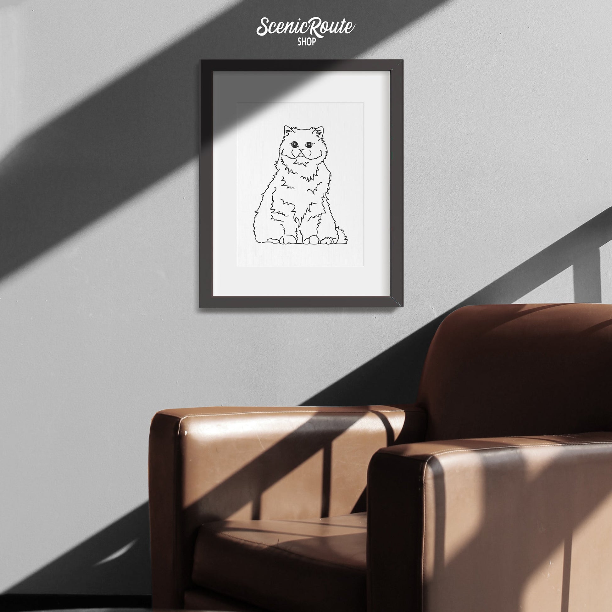 A framed line art drawing of a Persian cat above a leather chair