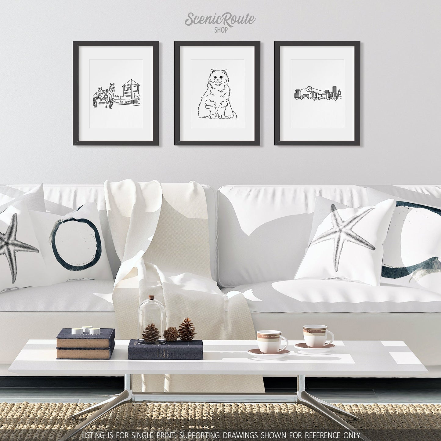 A group of three framed drawings on a white wall hanging above a couch with pillows and a blanket. The line art drawings include Harness Racing, a Persian cat, and the Portland Skyline