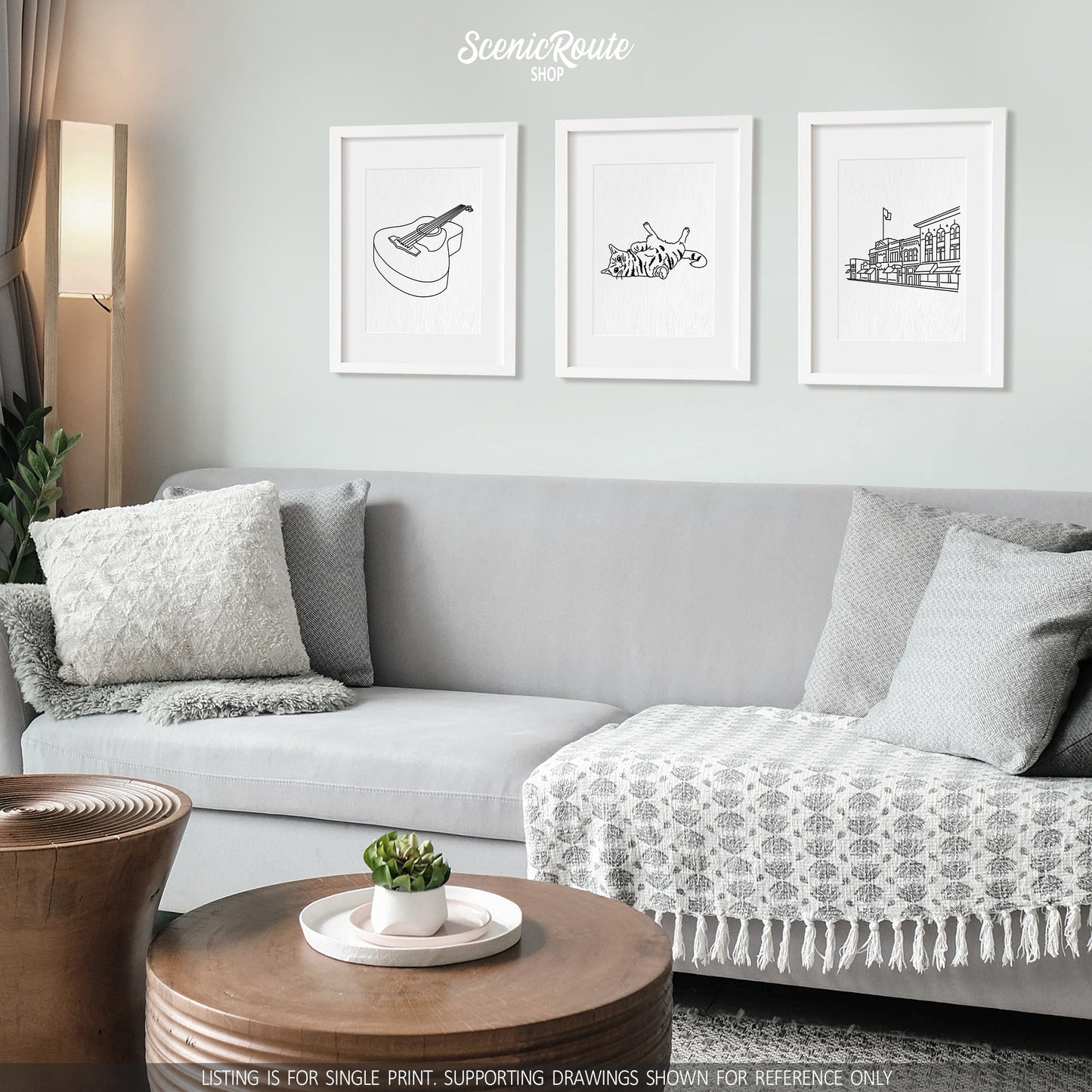 A group of three framed drawings on a white wall hanging above a couch with pillows and a blanket. The line art drawings include a Guitar, a Playful Cat, and the Prescott Skyline