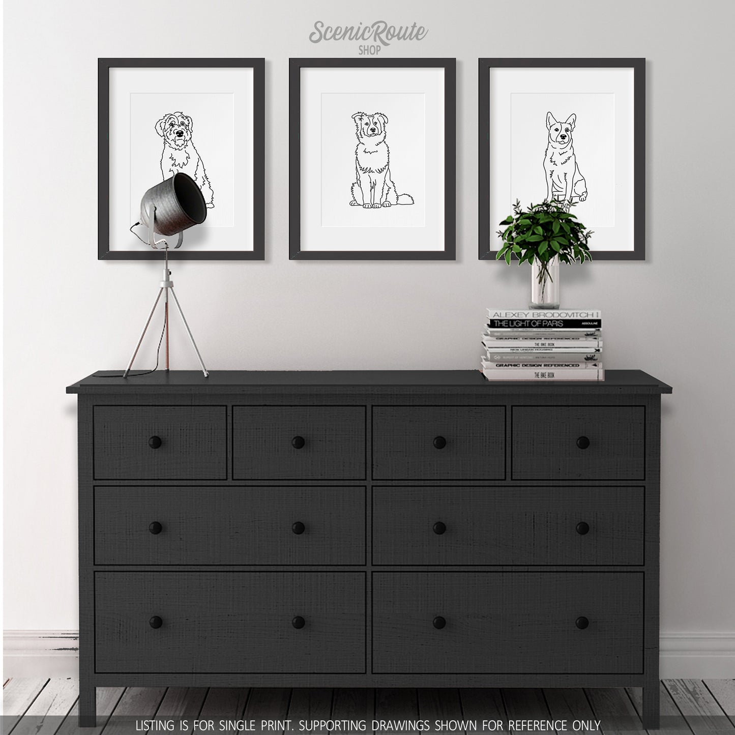 A black dresser with a lamp and a plant on top and three framed art prints hung above. The line art drawings include a Wheaten Terrier dog, Australian Shepherd dog, and Australian Cattle Dog