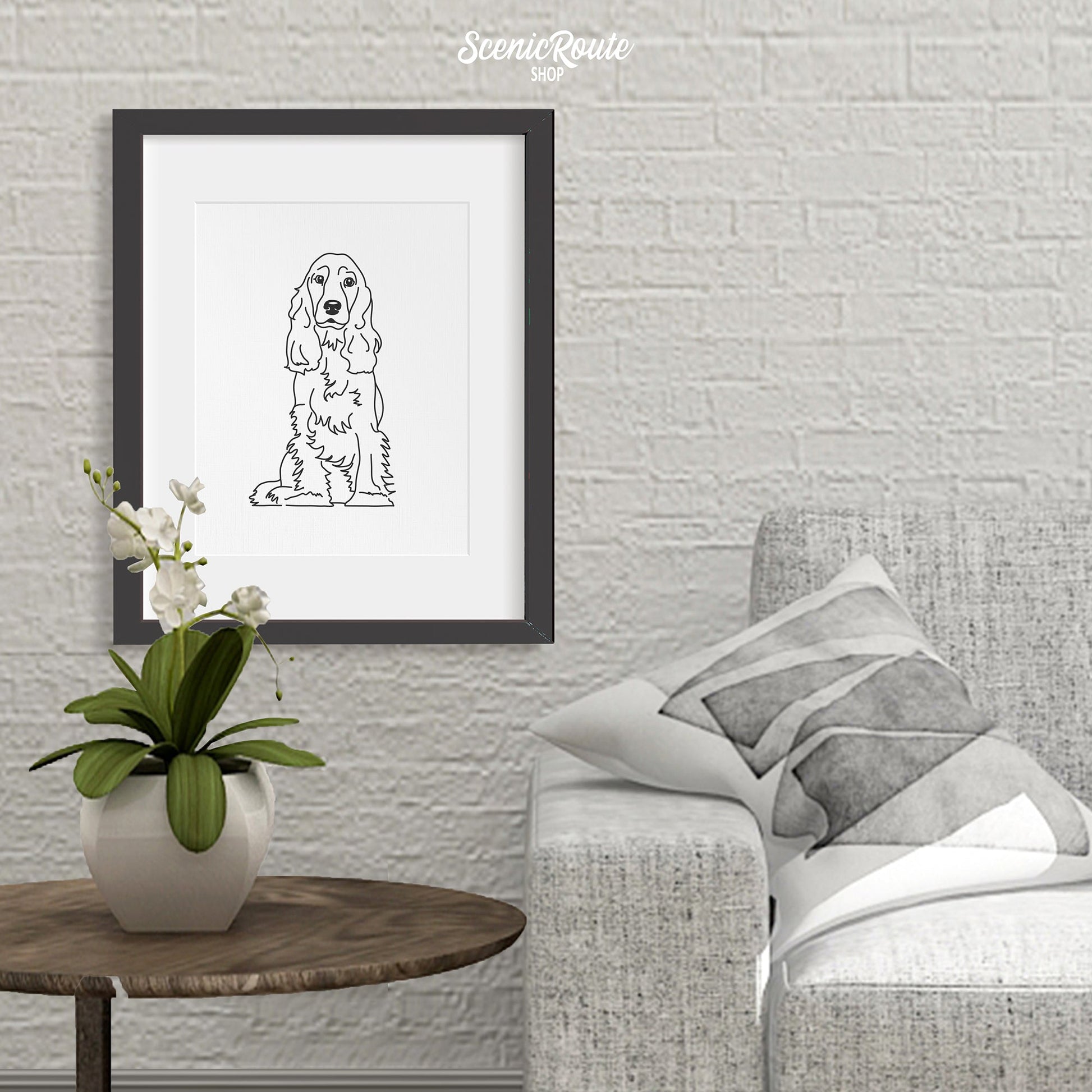 A framed line art drawing of a Cocker Spaniel dog on a brick wall hanging above a side table and plant next to a couch