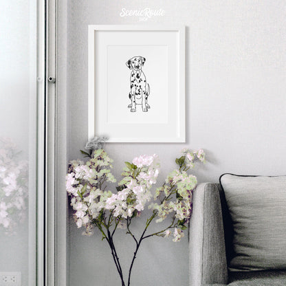A framed line art drawing of a Dalmatian dog above a flowering plant next to a couch