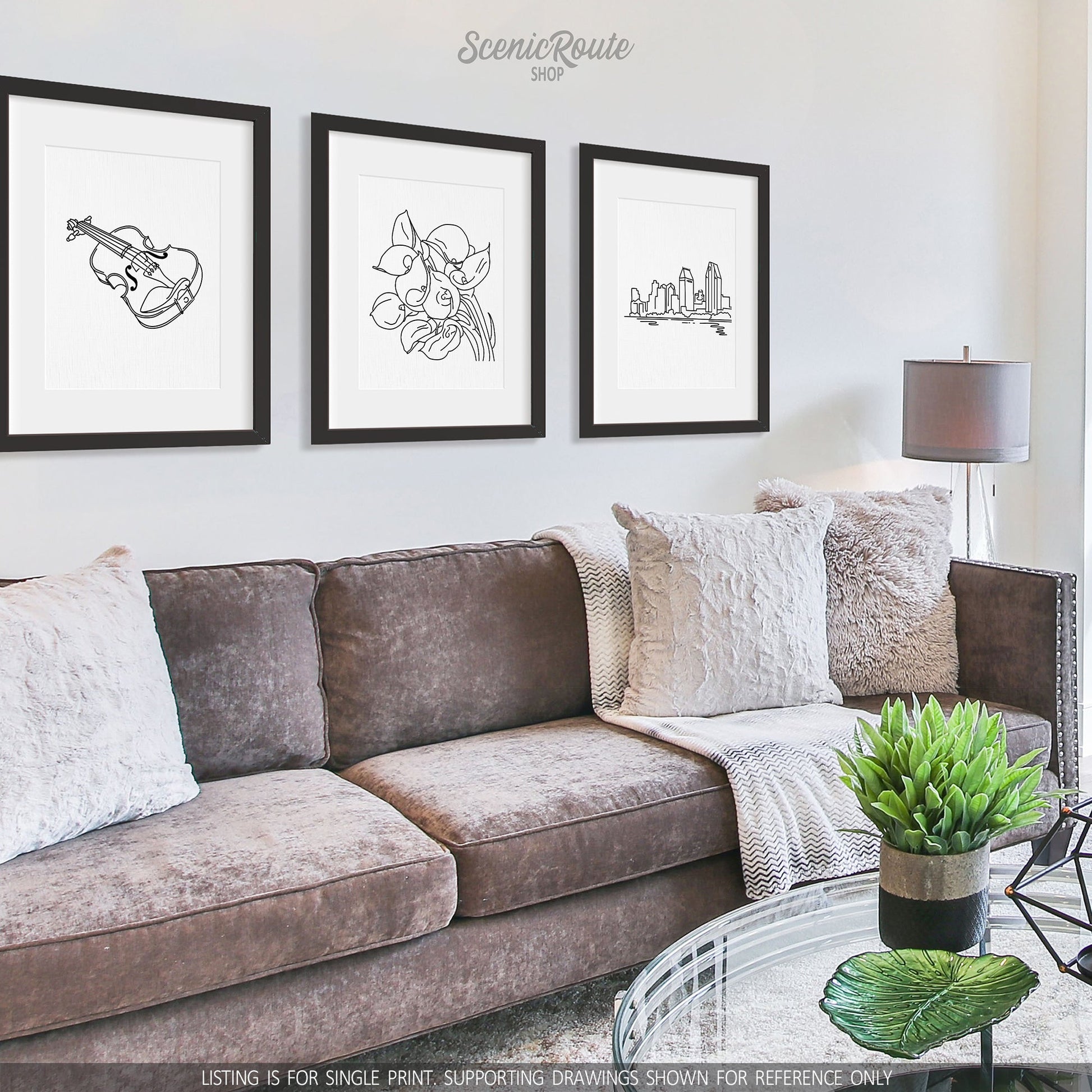 A group of three framed drawings on a white wall hanging above a couch with pillows and a blanket. The line art drawings include a Violin, Calla Lily Flower, and San Diego Skyline