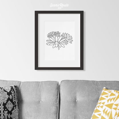 A framed line art drawing of a Daisy Flower hung above a couch