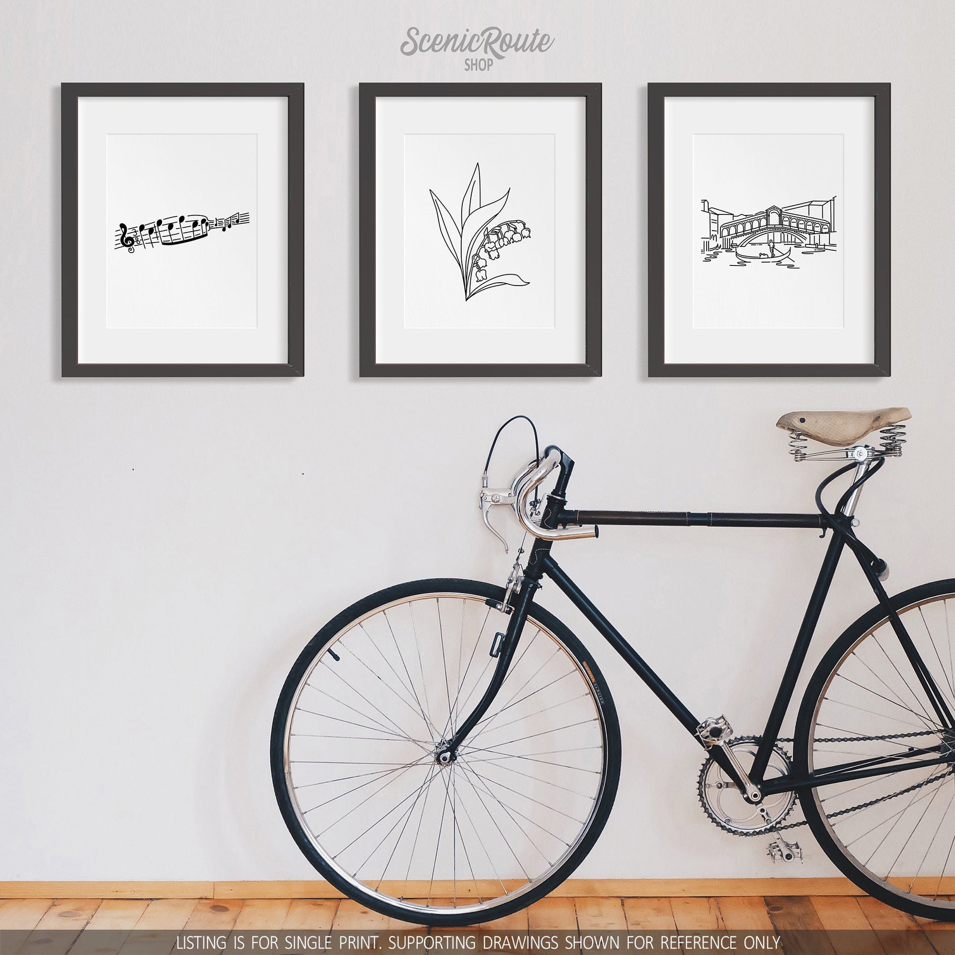 A group of three framed drawings on a white wall above a bicycle. The line art drawings include Music Notes, Lily of the Valley Flower, and the Rialto Bridge