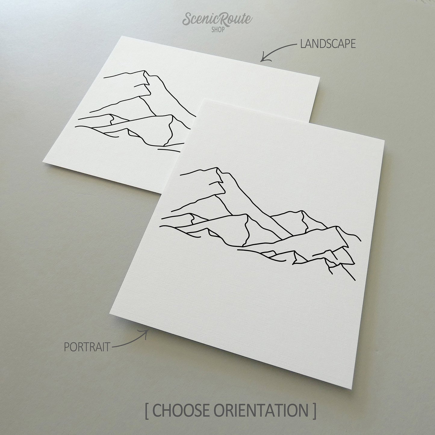 Two line art drawings of A Mountain Range on white linen paper with a gray background. The pieces are shown in portrait and landscape orientation for the available art print options.