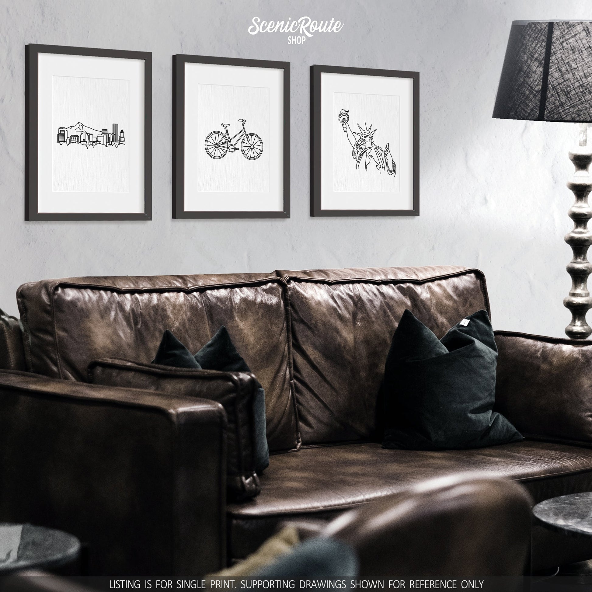 A group of three framed drawings on a wall above a dark leather couch. The line art drawings include the Portland Skyline, a Bicycle, and the Statue of Liberty