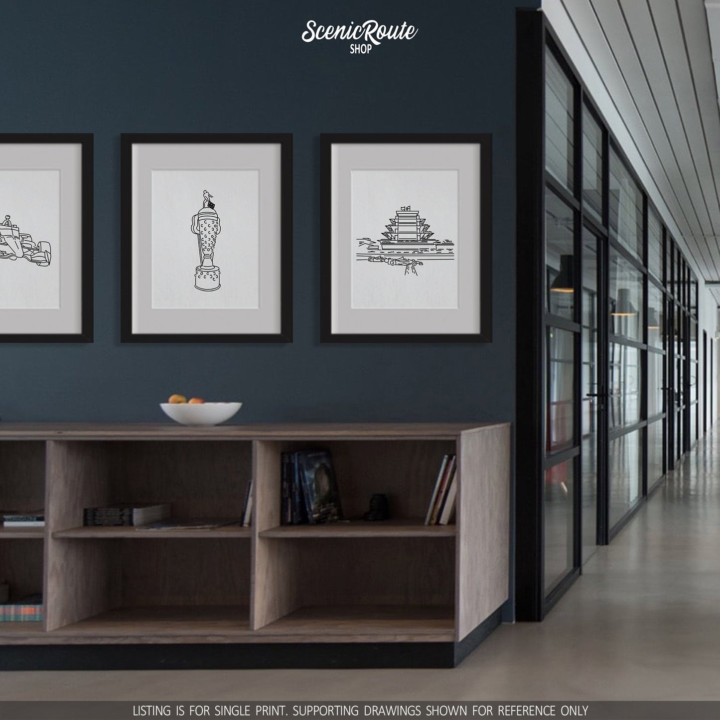 A group of three framed drawings on the wall above a cabinet in a modern office. The line art drawings include an Indy Car, the Indy Car Borg Warner Trophy, and the Speedway Pagoda