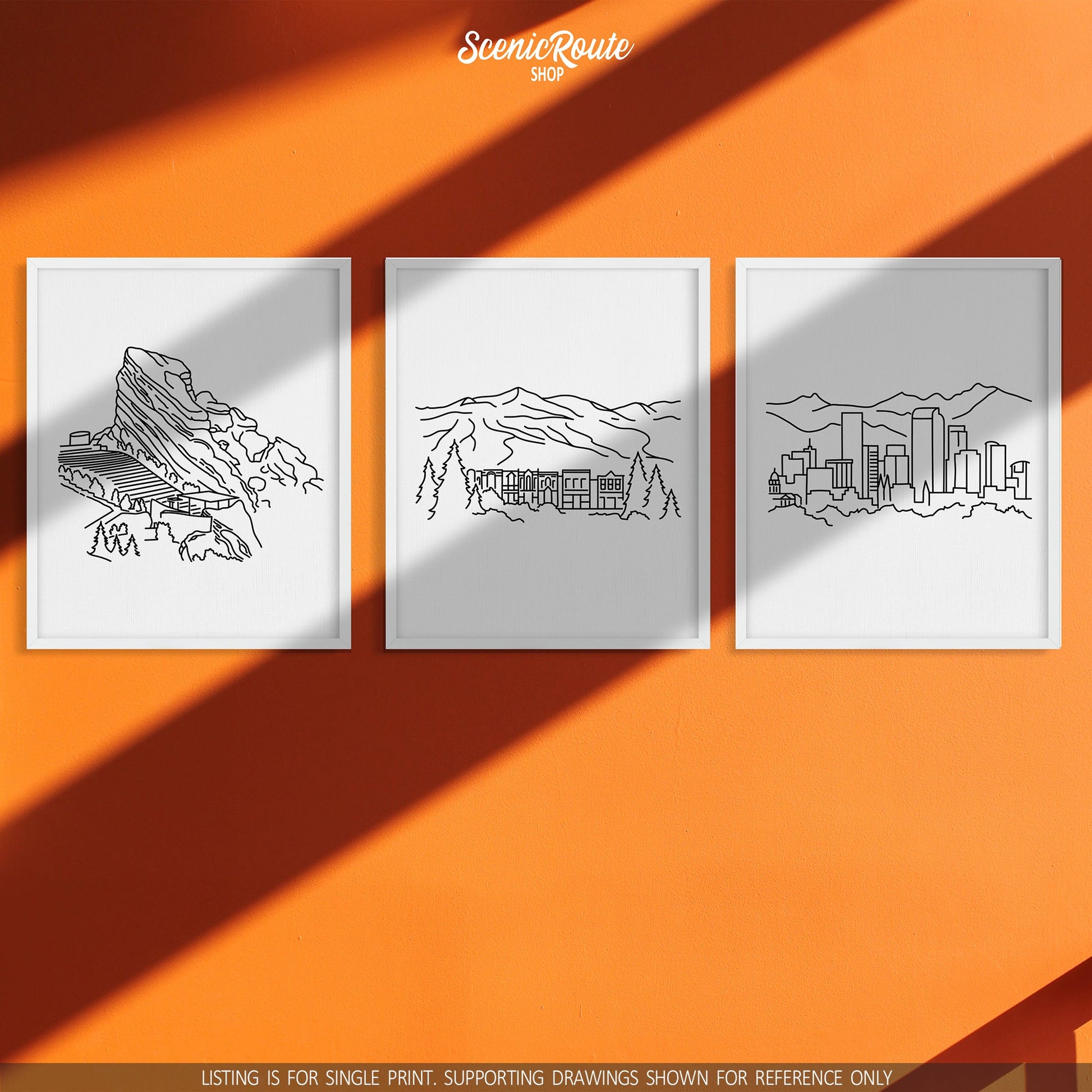 A group of three framed drawings on an orange wall. The line art drawings include Red Rocks Amphitheatre, Breckenridge, and the Denver Skyline