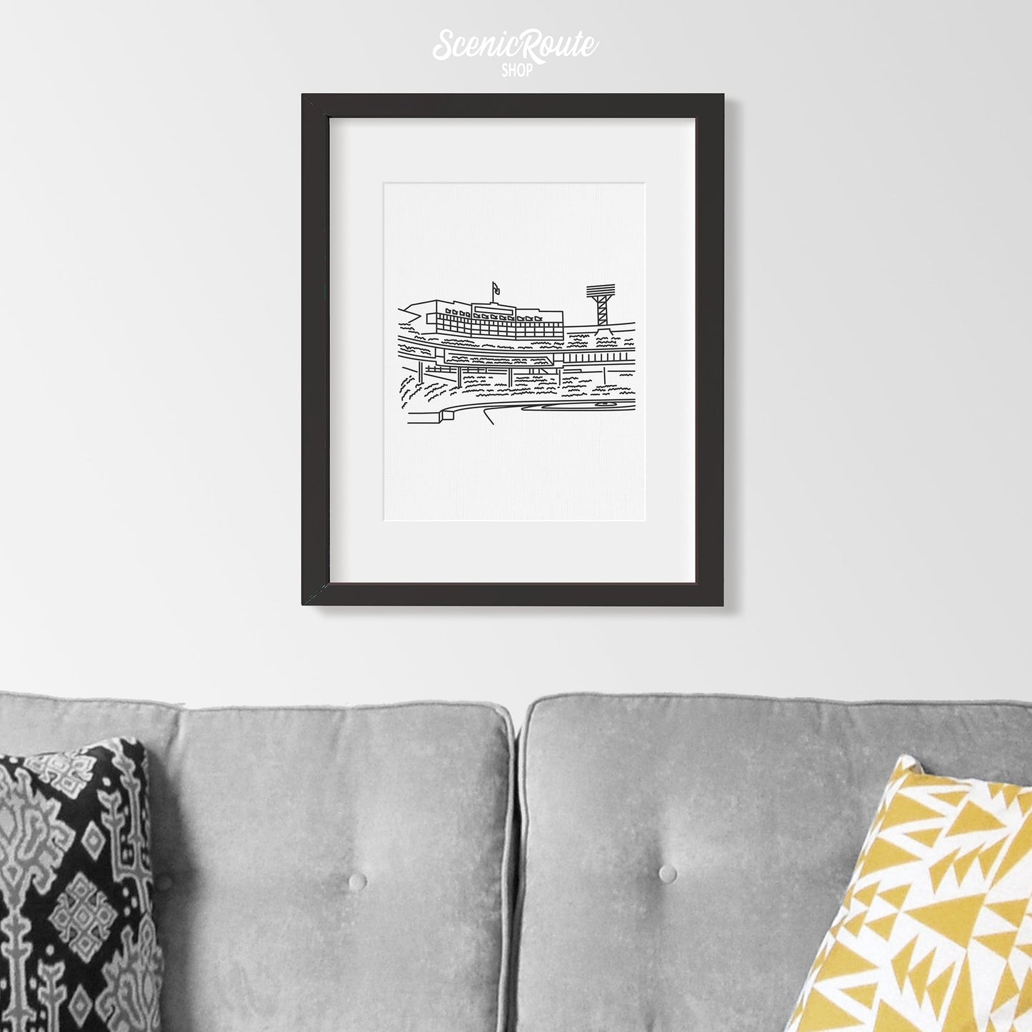 A framed line art drawing of Fenway Park hanging above a couch
