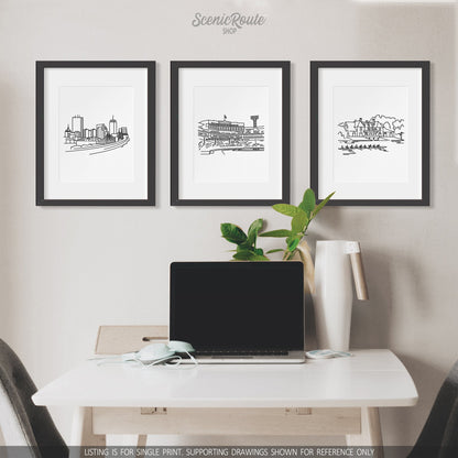 A group of three framed drawings on a wall above a desk with a laptop. The line art drawings include the Boston Skyline, Fenway Park, and Harvard Boathouse
