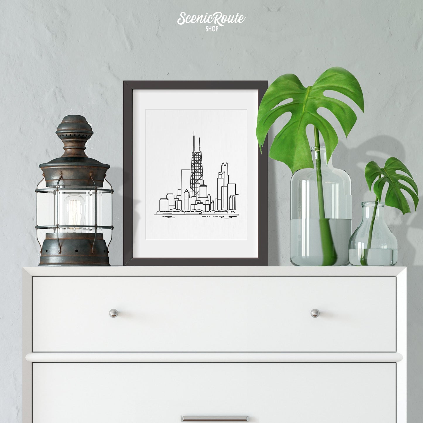 A framed line art drawing of the John Hancock Tower on a Dresser with vases and a lantern