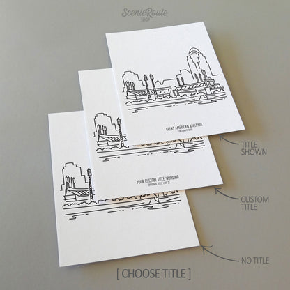 Three line art drawings of the Cincinnati Reds Ballpark in Ohio on white linen paper with a gray background.  The pieces are shown with title options that can be chosen and personalized.
