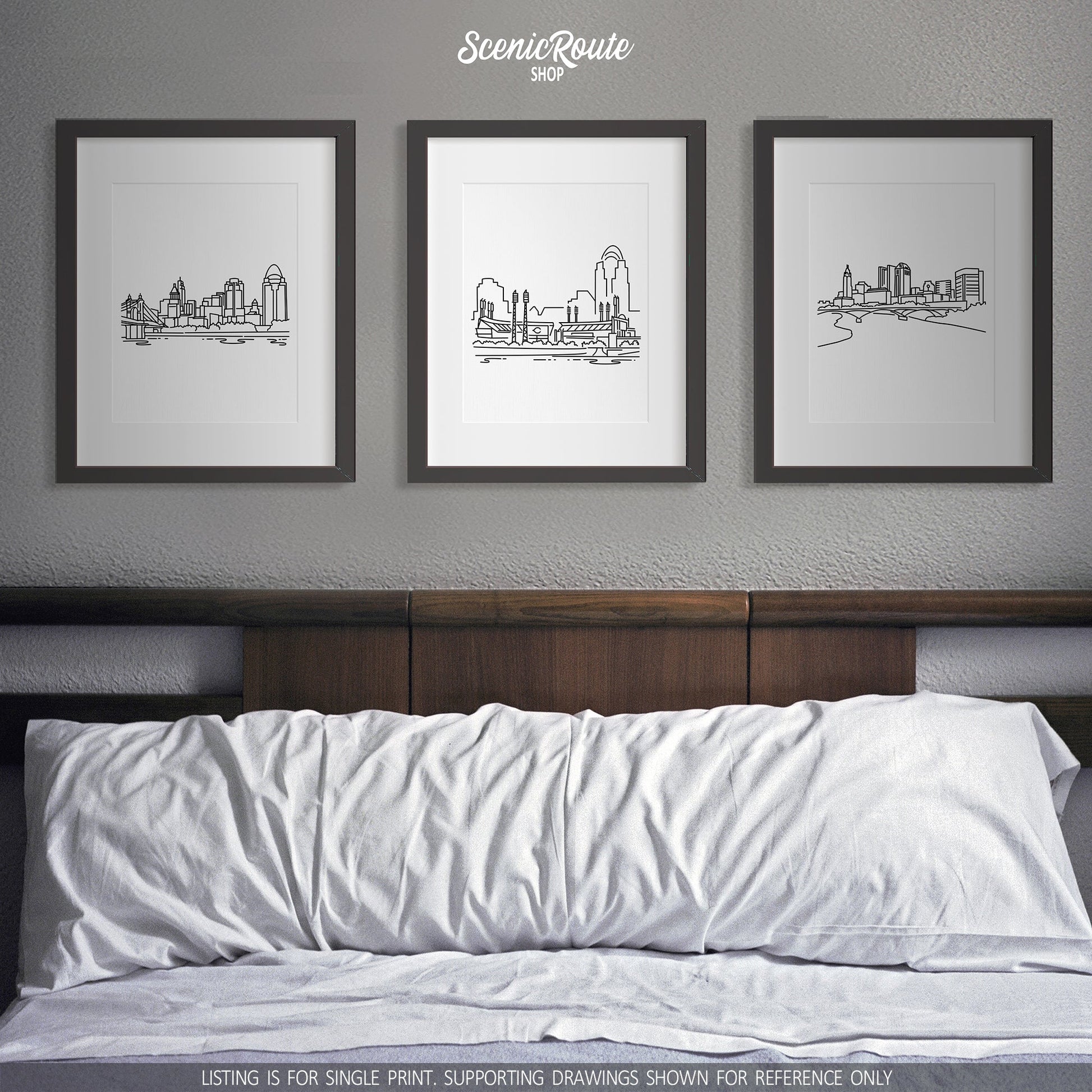 A group of three framed drawings on a white wall above a bed. The line art drawings include the Cincinnati Skyline, Cincinnati Reds Ballpark, and Columbus Skyline