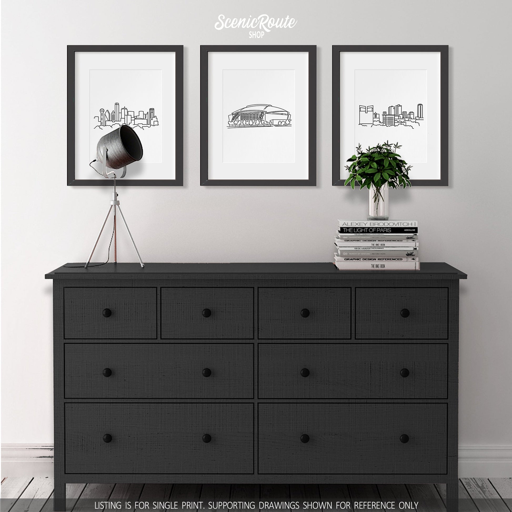 A group of three framed drawings hanging above a dresser with books and a plant. The line art drawings include the Dallas Skyline, Cowboys Stadium, and Fort Worth Skyline
