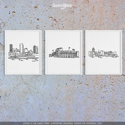A group of three framed drawings on a concrete wall. The line art drawings include the Milwaukee Skyline, Lambeau Field, and the Madison Skyline