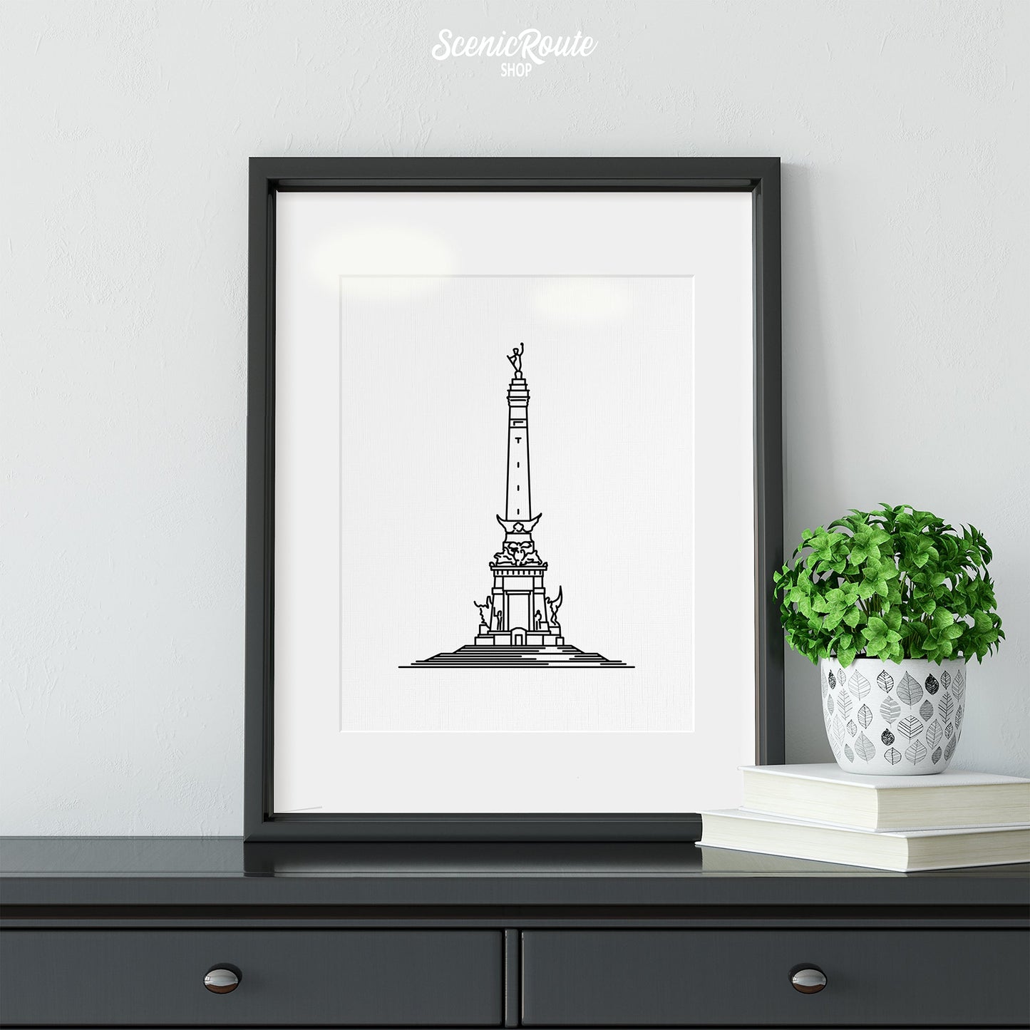 A framed line art drawing of the Soldiers and Sailors Monument on a dresser with a plant