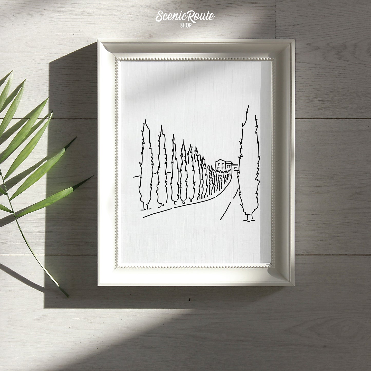 A framed line art drawing of a Tuscany Drive with a palm frond