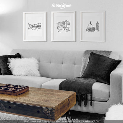 A group of three framed drawings on a white wall hanging above a couch with pillows and a blanket. The line art drawings include the Rialto Bridge, the Grand Canal, and the Florence Duomo