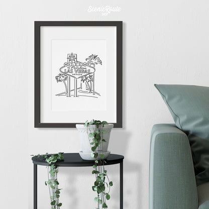 A framed line art drawing of the Las Vegas Sign above a small table with a plant