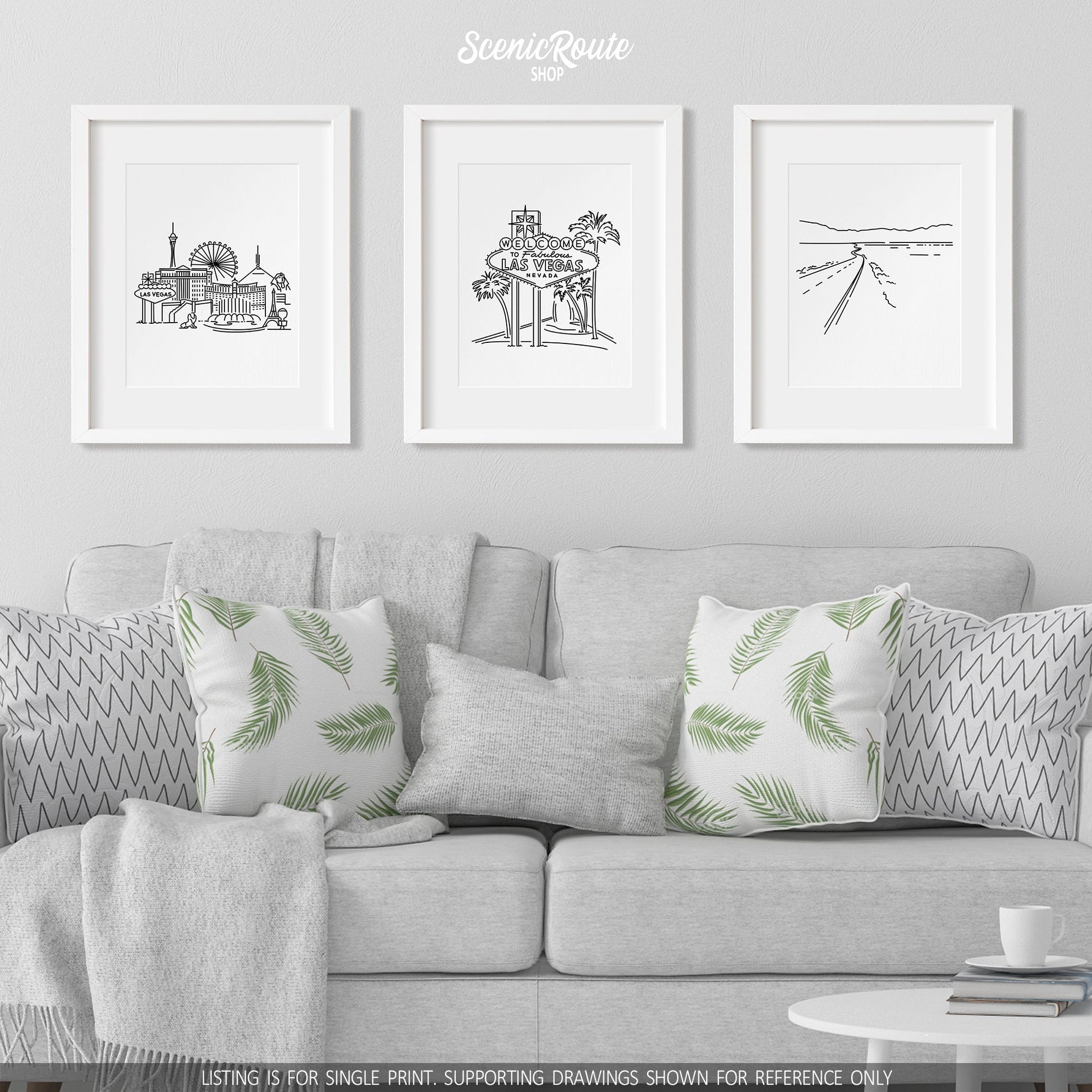 A group of three framed drawings on a white wall hanging above a couch with pillows and a blanket. The line art drawings include the Las Vegas Skyline, the Las Vegas Sign, and Death Valley National Park