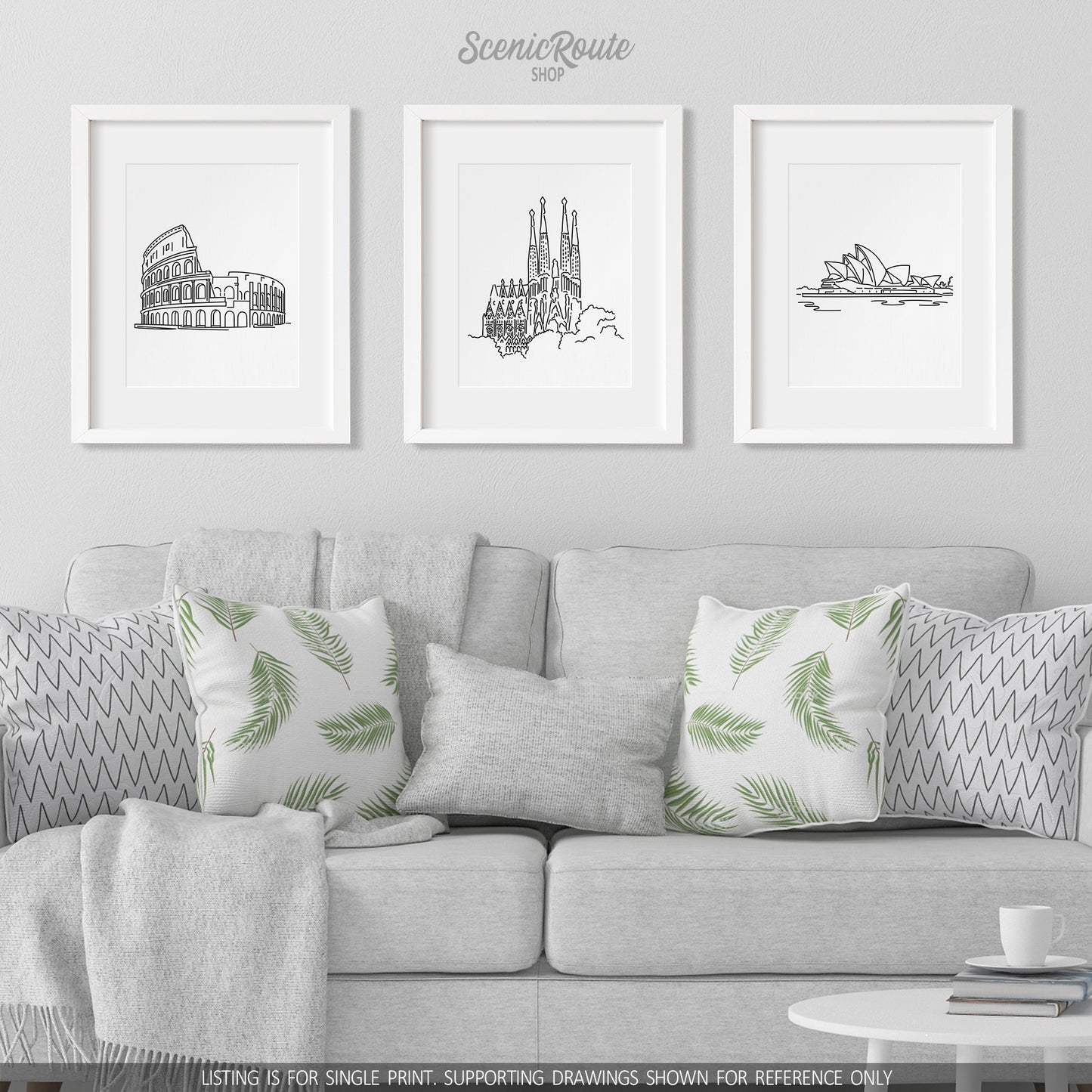 A group of three framed drawings on a white wall hanging above a couch with pillows and a blanket. The line art drawings include the Sydney Opera House, Sagrada Familia, and Colosseum