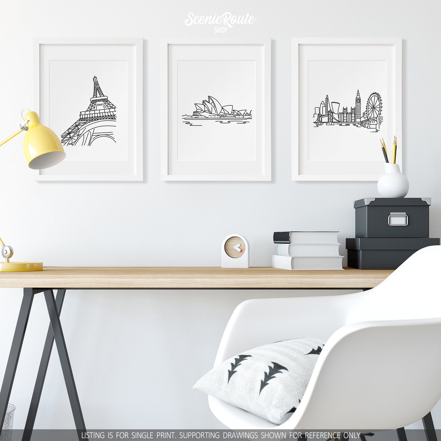 A group of three framed drawings on a wall above a desk. The line art drawings include the Eiffel Tower, Sydney Opera House, and London Skyline
