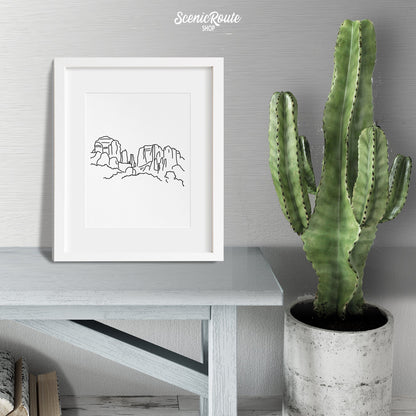 A framed line art drawing of Sedona Cathedral Rock on a wood bench next to a potted cactus