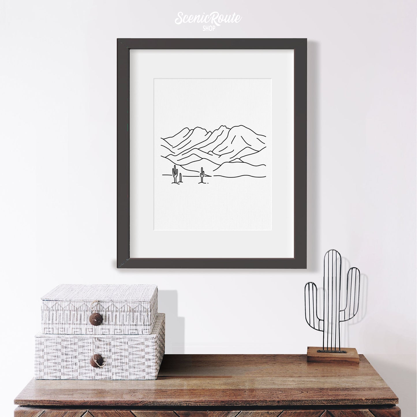 A framed line art drawing of Four Peaks Mountains above a table with saguaro figurine