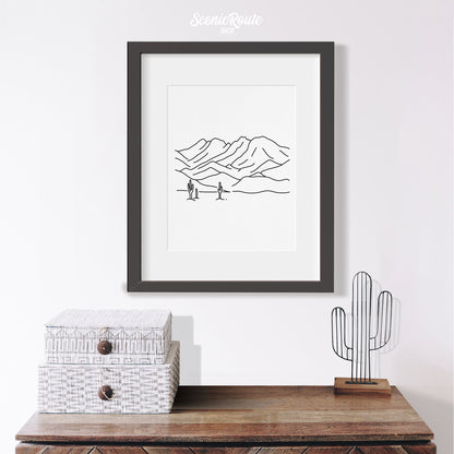A framed line art drawing of Four Peaks Mountains above a table with saguaro figurine