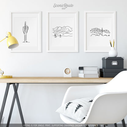 A group of three framed drawings on a wall above a desk. The line art drawings include a Saguaro Cactus, the Four Peaks Mountains, and the Superstition Mountains