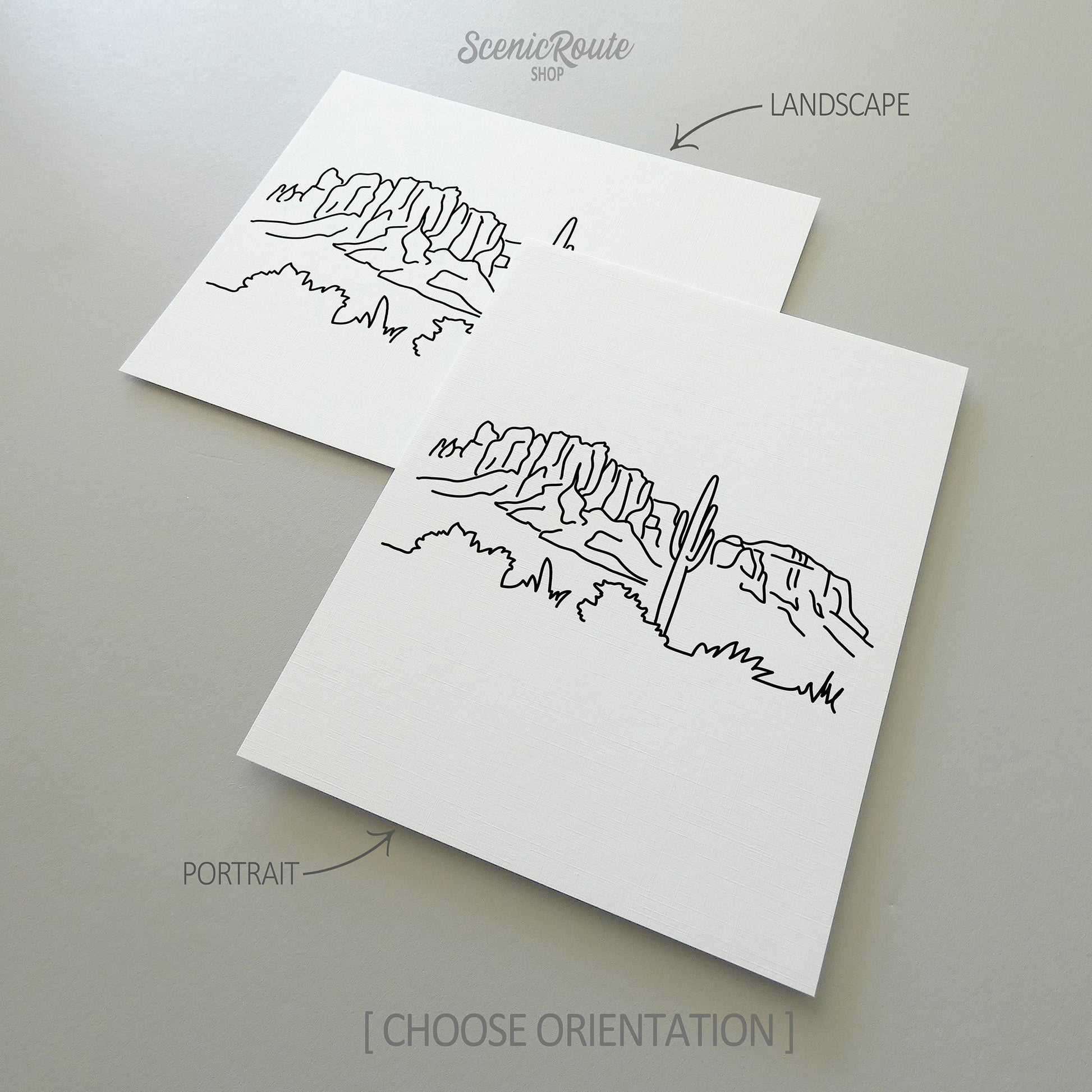 Two line art drawings of Superstition Mountains on white linen paper with a gray background.  The pieces are shown in portrait and landscape orientation for the available art print options.