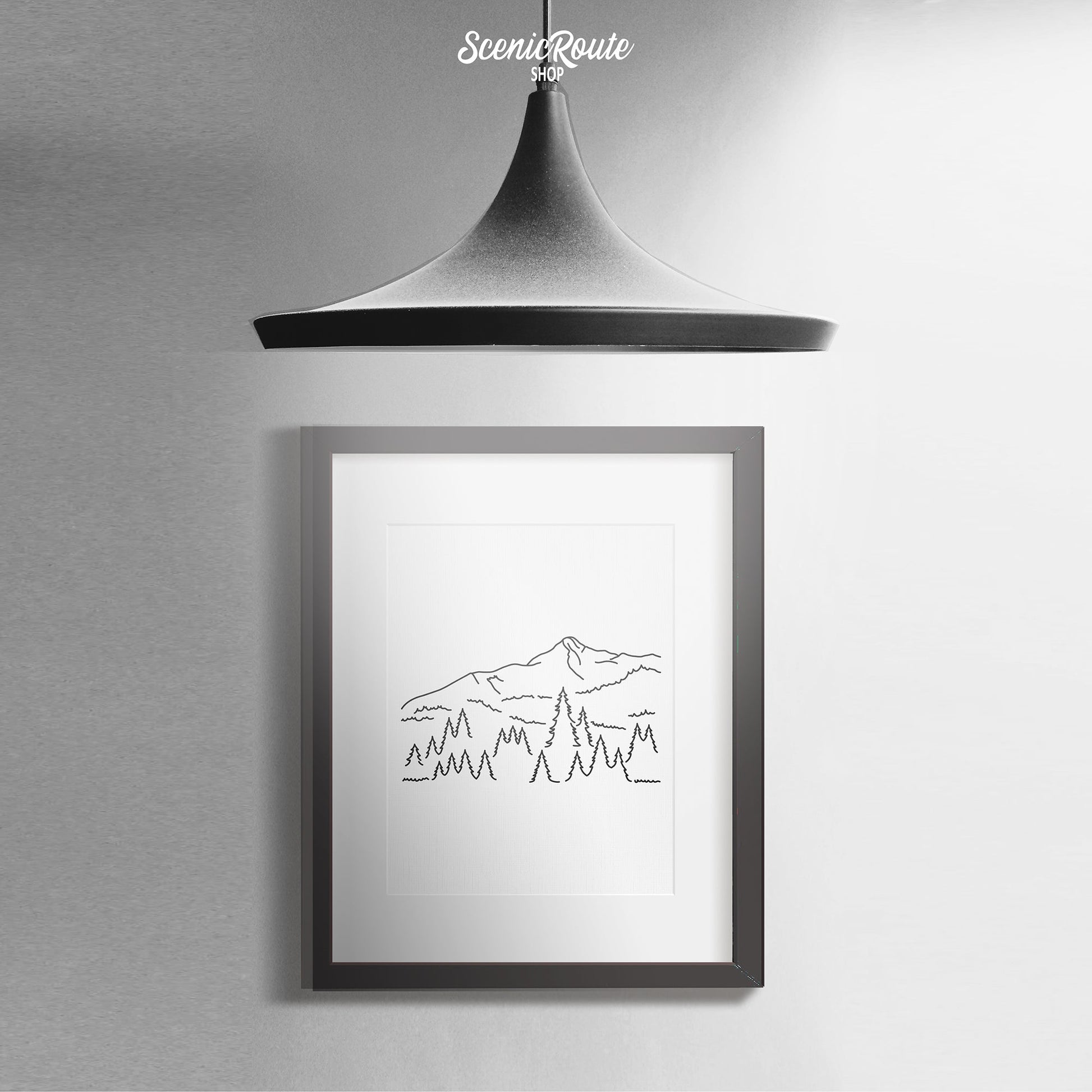 A framed line art drawing of Big Sky Montana with a light hanging above it