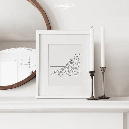 A framed line art drawing of Acadia National Park on a mantle with candles and a mirror