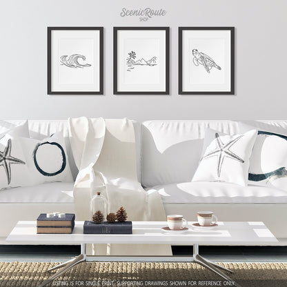 A group of three framed drawings on a wall above a couch. The line art drawings include Waves, American Samoa National Park, and a Sea Turtle