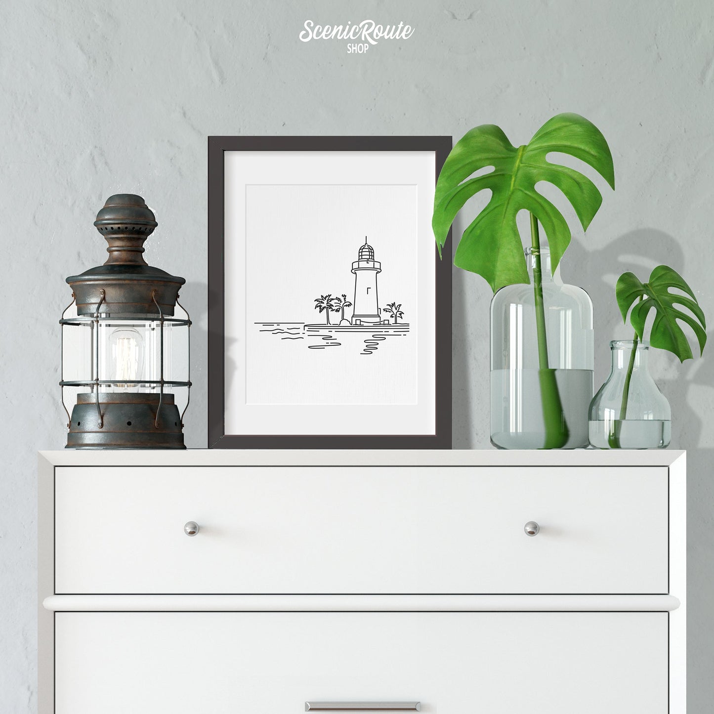 A framed line art drawing of Biscayne National Park on a white dresser with vases and lantern