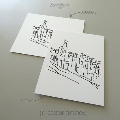 Two line art drawings of Bryce Canyon National Park on white linen paper with a gray background.  The pieces are shown in portrait and landscape orientation for the available art print options.