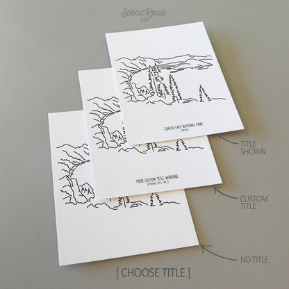 Three line art drawings of Crater Lake National Park on white linen paper with a gray background. The pieces are shown with title options that can be chosen and personalized.