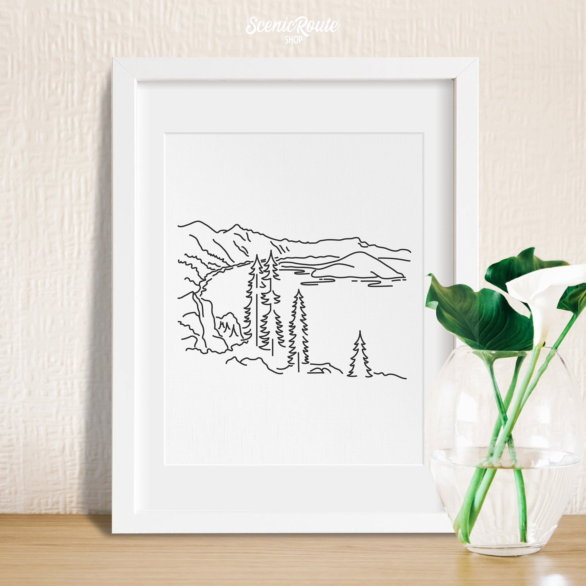 A framed line art drawing of Crater Lake National Park with a vase