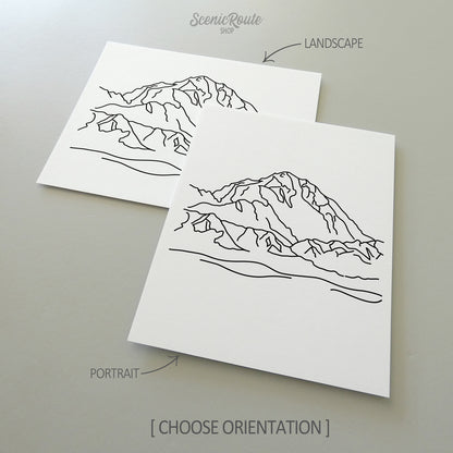 Two line art drawings of Denali National Park on white linen paper with a gray background.  The pieces are shown in portrait and landscape orientation for the available art print options.