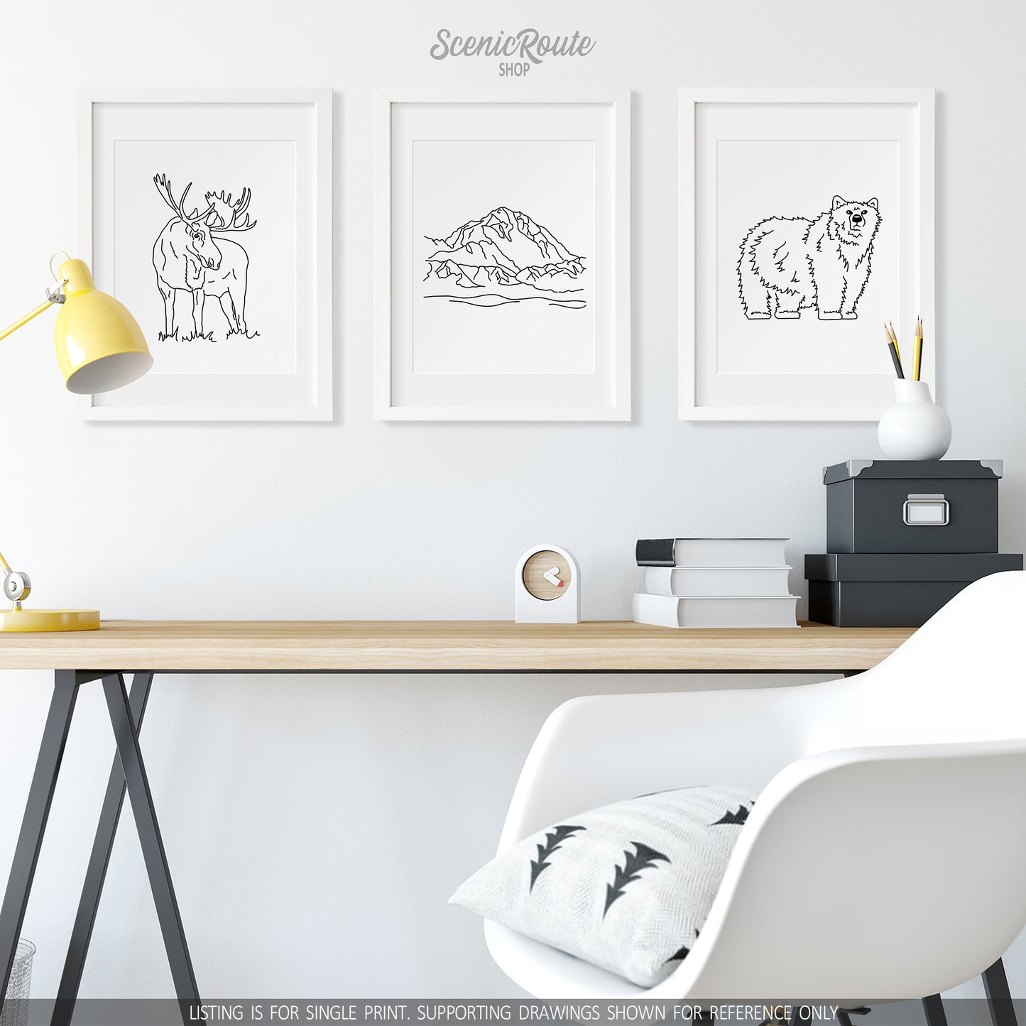 A group of three framed drawings on a wall above a desk. The line art drawings include a Moose, Denali National Park, and a Grizzly Bear