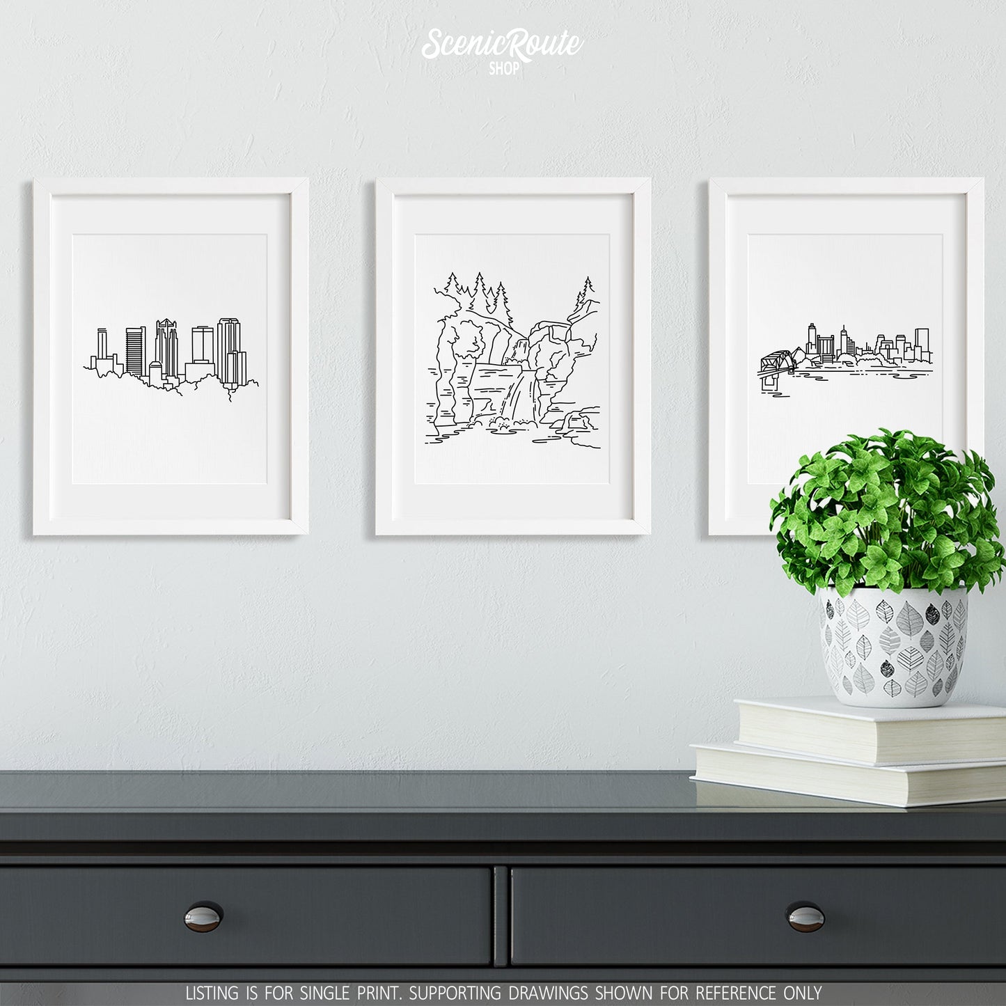 A group of three framed drawings on a wall above a dresser with books and a plant. The line art drawings include the Birmingham Skyline, Hot Springs National Park, and the Memphis Skyline