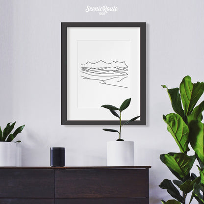 A framed line art drawing of White Sands National Park hanging above a dresser with plants